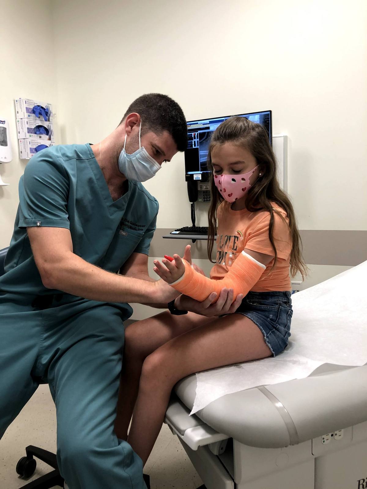 Dr. Goldwaser signing a young patient’s orange cast while she watches